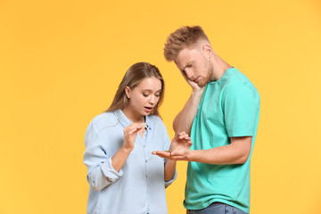 Troubled couple counting coins against color background