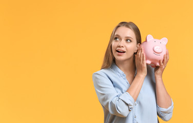 Young woman with piggy bank on color background