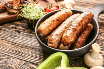 Frying pan with tasty grilled sausages on wooden table
