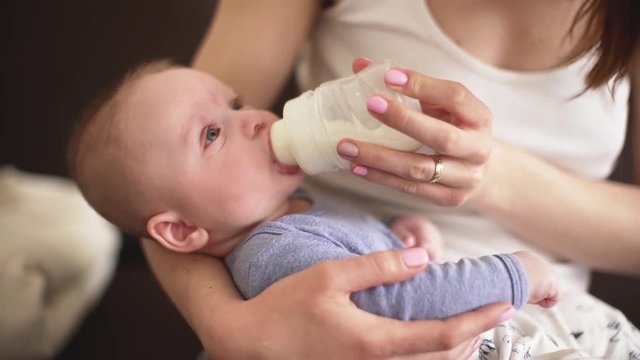 Mother holding 4 months old infant boy, feeding him milk from bottle