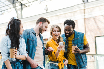 cheerful multicultural friends looking at smartphone while standing together