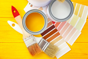 Cans of paint with brushes and palette samples on wooden background
