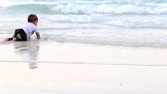 Baby boy crawling on the wave of the sea on the sand beach