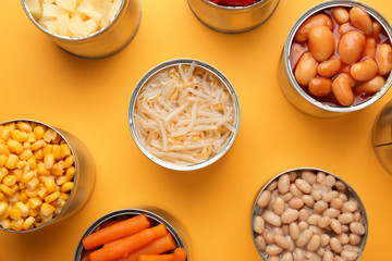 Tin cans with different food on color background
