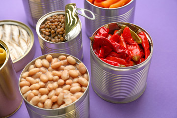 Tin cans with different food on color background