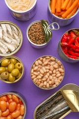 Tin cans with different food on color background