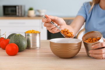 Woman taking beans from tin can at table in kitchen