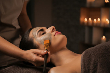 Cosmetologist applying mask on woman's face in spa salon