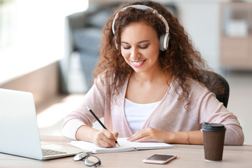 Young African-American student listening to music while preparing for exam