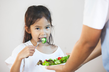 Mother give a bowl of salad to asian child girl to eat healthy vegetables for her meal