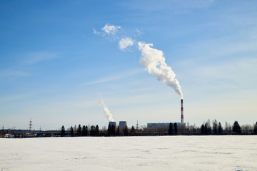Winter landscape with snowy field and factory with large pipes from which white smoke goes