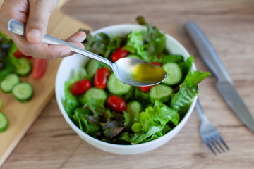 Asian woman pouring olive oil into  fresh vegetable salad bowl in the kitchen