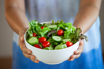 Asian woman holding salad bowl and eating healthy vegetables