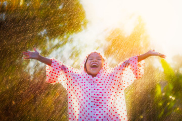 Happy asian child girl wearing raincoat having fun to play with the rain in the sunlight