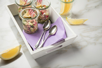 Norddeutscher Friesischer Nordseekrabben Salat Glas Becher mit Gurken, Radieschen, Zwiebeln, Dill und Zitronen auf Holz Tablett und Marmor Tisch