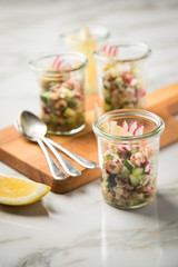 Norddeutscher Friesischer Nordseekrabben Salat Glas Becher mit Gurken, Radieschen, Zwiebeln, Dill und Zitronen auf Holz Brett und Marmor Tisch