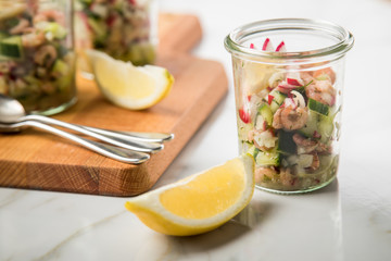 Norddeutscher Friesischer Nordseekrabben Salat Glas Becher mit Gurken, Radieschen, Zwiebeln, Dill und Zitronen auf Holz Brett und Marmor Tisch