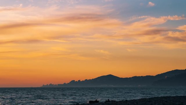 Beautiful scarlet sunset on the Black Sea coast in the city of Sochi. Time lapse 4k. Clouds that are painted in sunset color are floating over the silhouettes of buildings in the distance.