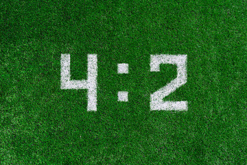 Football score 4:2.White numbers four and two are drawn on the green grass,creative scoreboard