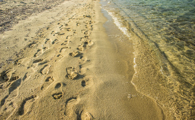 vintage style toning photography of sand beach summer vacation destination place with human bare foot prints on a ground and transparent sea water 