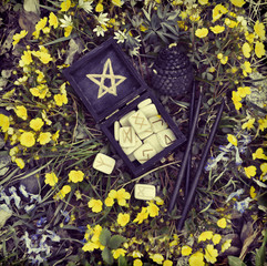 Black box with wooden runes and candles in flowers.
