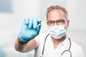 Pharma Scientist or doctor with medical face mask and gloves shows a medicin pill in his hand