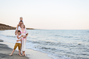 Happy family of four hugging on the sea coast. Parents, pregnant mother and two sons.