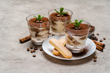 Obraz na płótnie Canvas Classic tiramisu dessert in a glass cup and savoiardi cookies on plate on concrete background