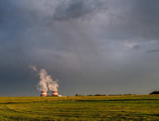 Mown field, grey overcast cloudy sky and steaming cooling towers over horizon