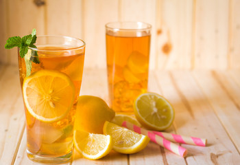 Glasses of ice tea with lemon slices and mint on wooden background
