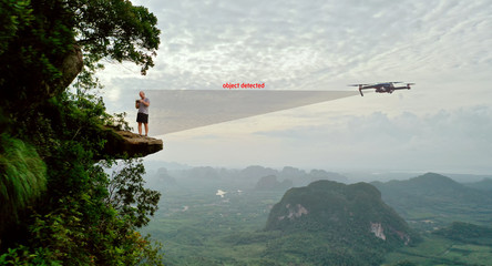 Aerial view of man drone operator on the edge of the rock over beautiful green mountains and sky background. Drone detection analytics, future technology concept
