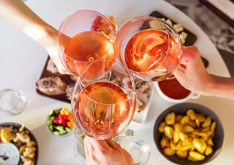 Hands holding glasses with rose wine over the table with food.