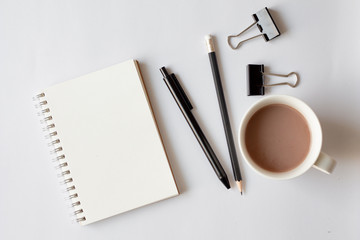 Creative flat lay photo of work space desk with notebook, cup of coffee, pen, pencil and paper clip on white background, minimal style. 