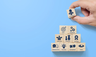 Hand arranging wood block stacking pyramid with icon leader business on blue background. Key success factors for leadership elements concept - obrazy, fototapety, plakaty