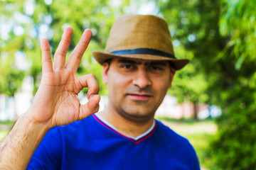 man in hat shows hand gesture OK  on nature background