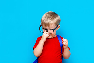 small smiling schoolboy on blue background in glasses toutch his glasses. back to school, preschool kid
