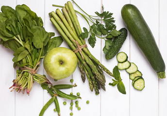 Green vegetables and herbs on the white wooden background, top view