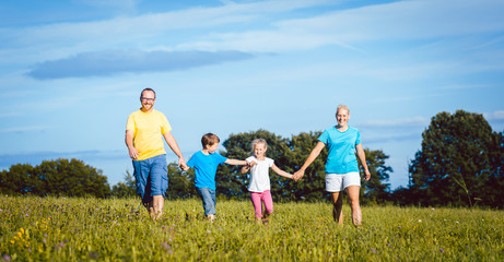 Fototapeta premium Family holding hands running over meadow