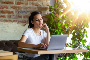Woman working on laptop at a cafe. Young woman working on a laptop. Beautiful young woman working with laptop from coffee shop. Attractive woman sitting in a cafe with a laptop