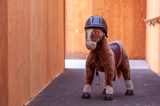 Large plush brown toy horse in a black riding helmet standing on a walkway in a barn