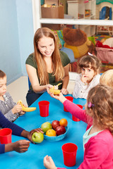 Teacher and children eat fruit in the day care center