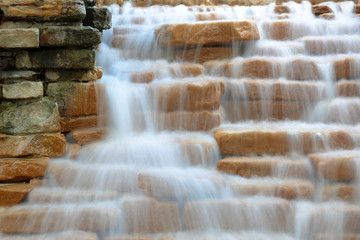 Up close view at decorative waterfall in a park of San Antonio, Texas. Water flowing down the yellow steps stones