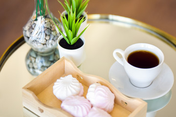A Cup of tea and delicious pink cakes are on the table. Potted plant on the table. Breakfast.