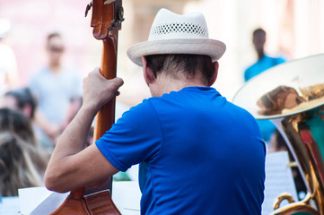 Portrait of contrabassist with hat on back view playing in band  in tne street