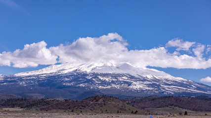 Mount Shasta, California with clouds on a sunny day against bright blue sun from I-5 interstate
