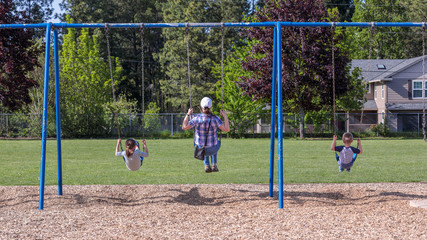 Hillsboro, Oregon \ USA - 04 May 2019: Happy family - mother with two kids - a boy and a girl on a swing in a park