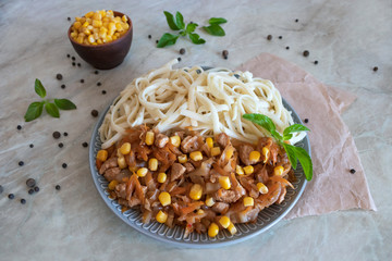 Noodles with vegetables in a large plate. Corn grains in the bowl. Traditional healthy oriental food on the table.