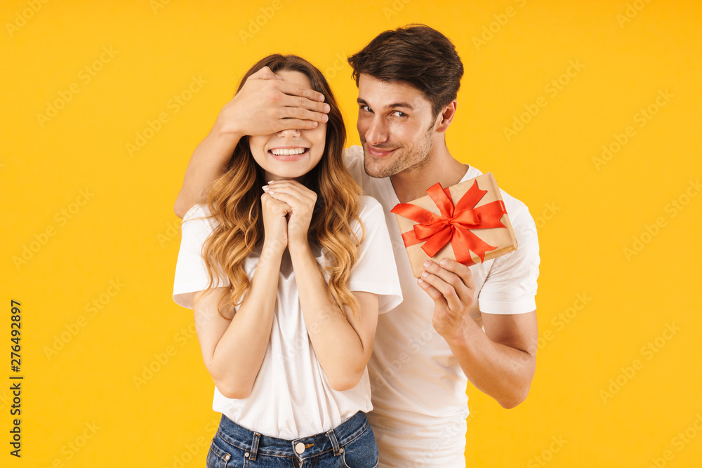 Wall mural portrait of caucasian couple in basic t-shirts standing together while man holding present box and c