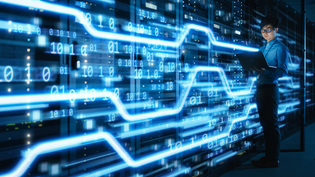Shot of Asian IT Specialist Using Laptop in Data Center Full of Rack Servers. Concept of High Speed Internet Connections with Blue Visualization Projection of Data Transmission with Digits.