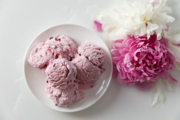 Balls of berry ice cream on a plate and white and pink peonies on a white background top view